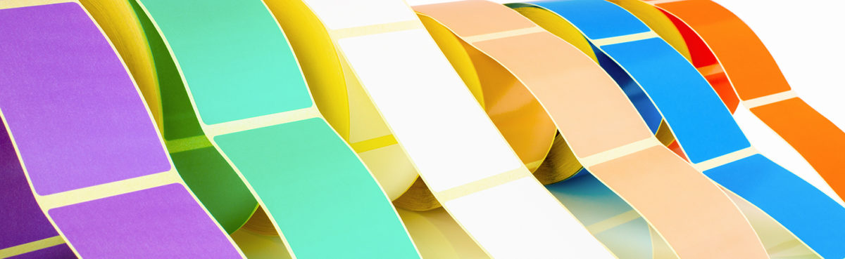 Plain Adhesive Labels on rolls in various colours including purple, green, yellow, white, blue, orange, and peach, displayed in a curved arrangement.