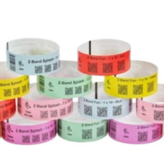 Stacked rolls of Zebra Z-Band Fun wristbands in bright colours, including red, orange, yellow, green, blue, pink, and purple, featuring QR codes and space for printable information, designed for event and patient identification.