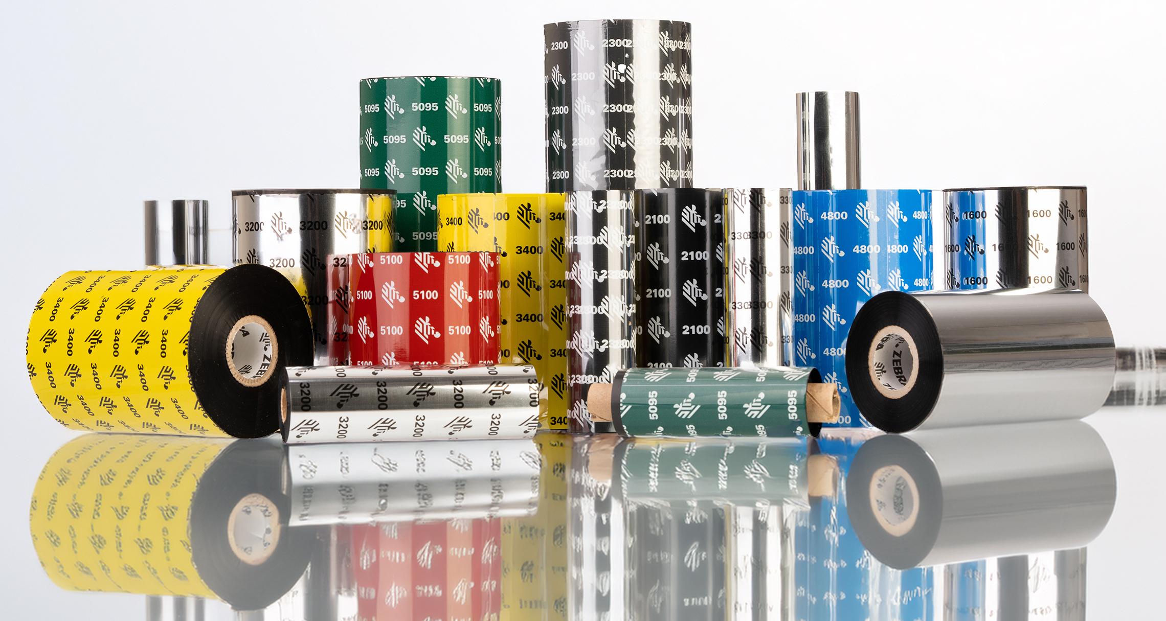 Assorted Genuine Zebra thermal transfer ribbons in various colors and sizes, featuring branding and product codes like 3200, 3400, 4800, and 5095, displayed with reflective surfaces.